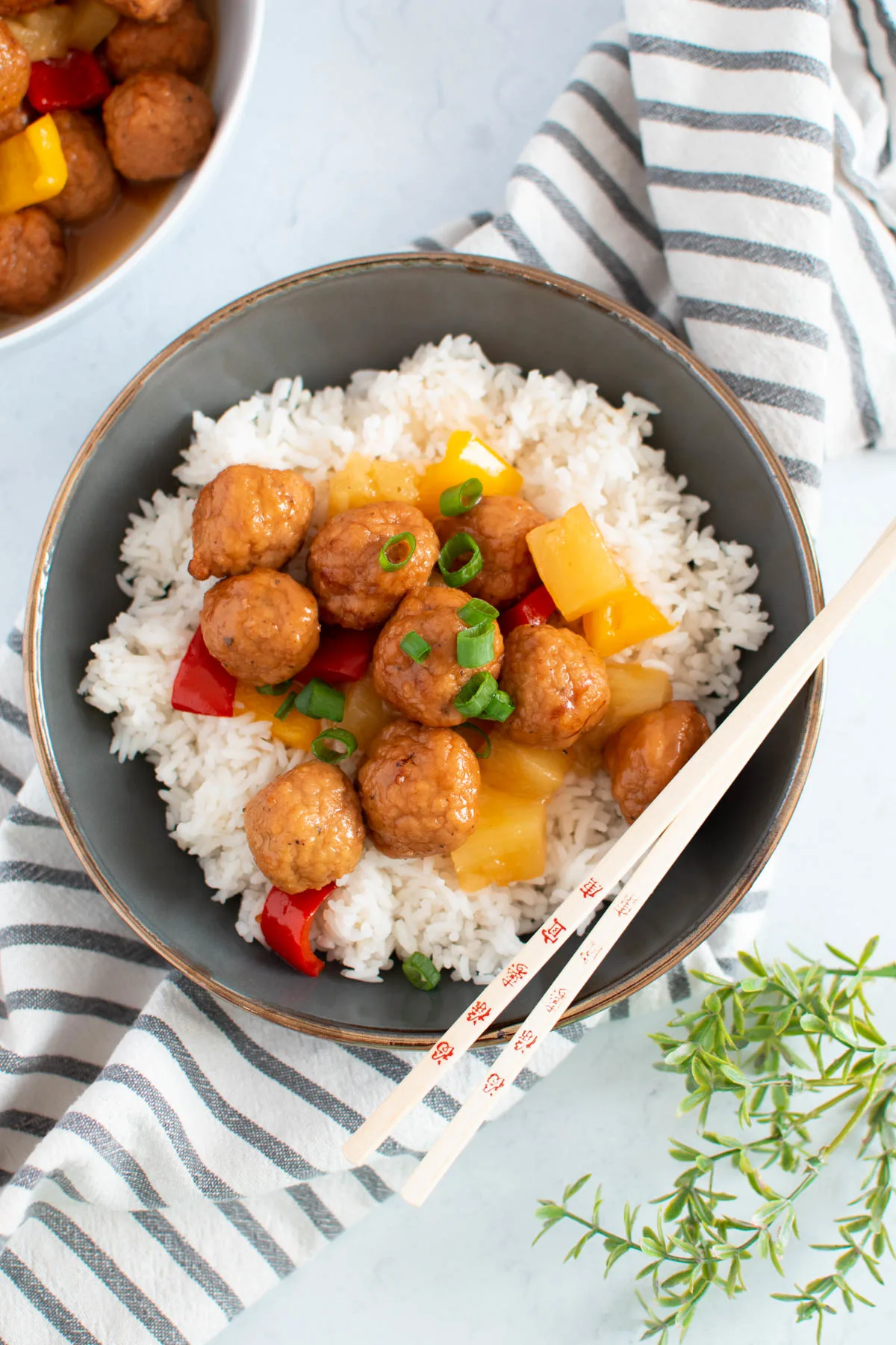 Sweet and sour meatballs over cooked white rice in gray bowl with chopsticks laying on bowl.