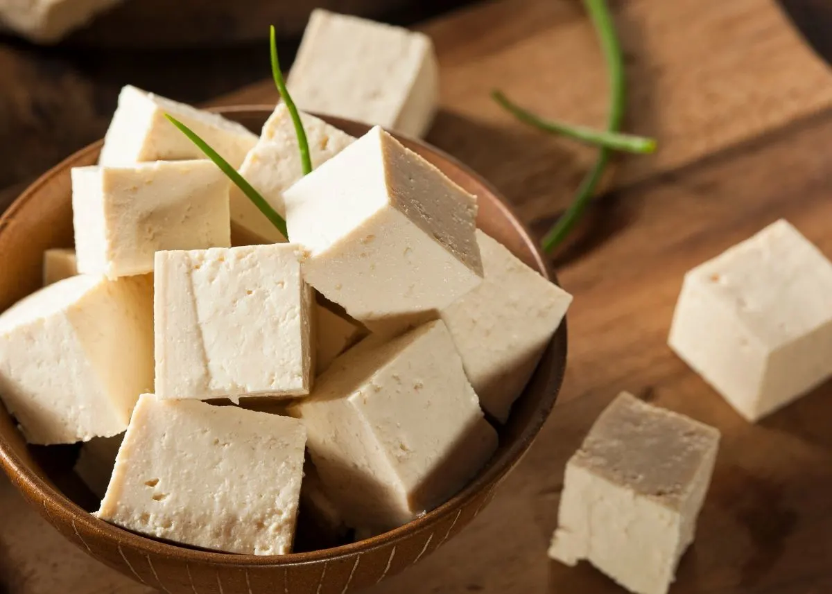 Cubes of tofu piled in a brown bowl on cutting board with green garnish.