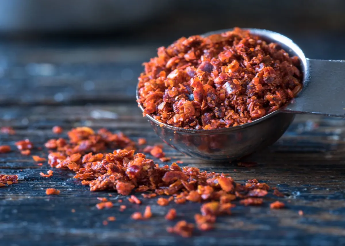 Small metal bowl filled with aleppo pepper flakes on a rustic wooden table.