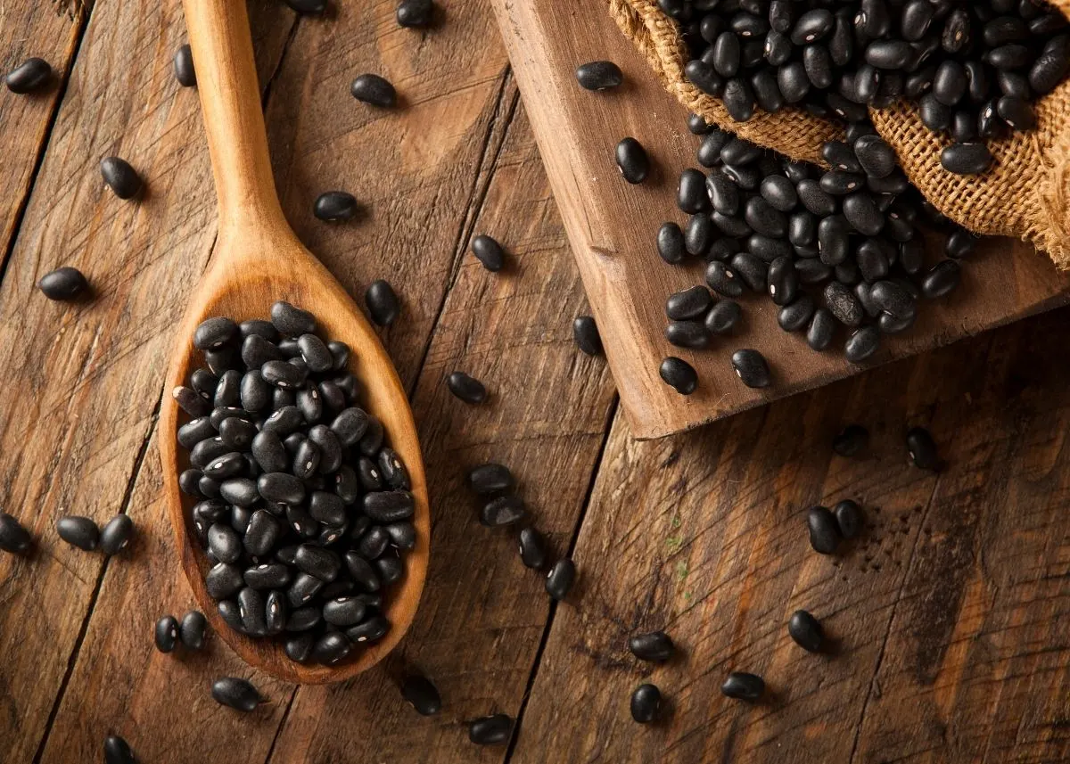 Black beans on a large wooden spoon and wooden cutting board with burlap.