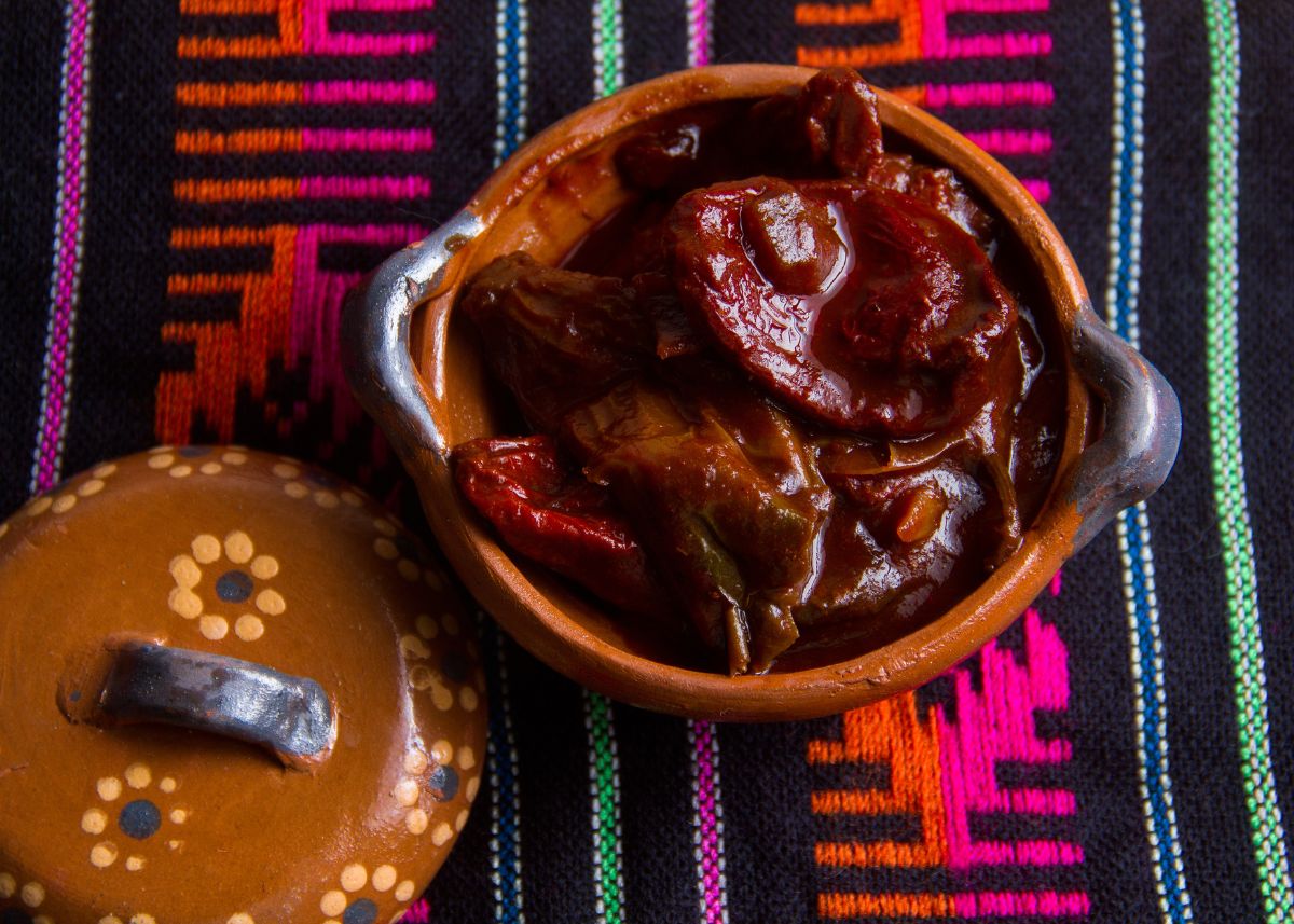 Clay pot filled with chipotle peppers in adobo sauce on a colorful Mexican cloth.