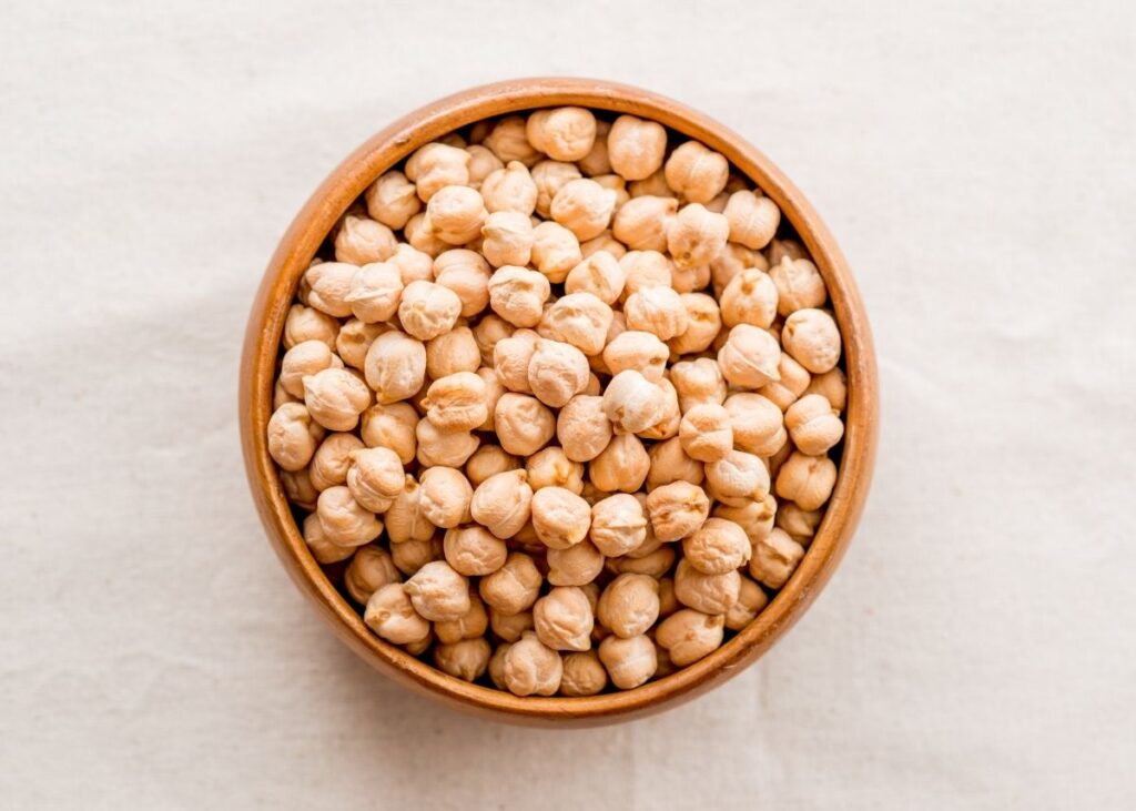 Large wooden bowl filled with garbanzo beans on a tan background.