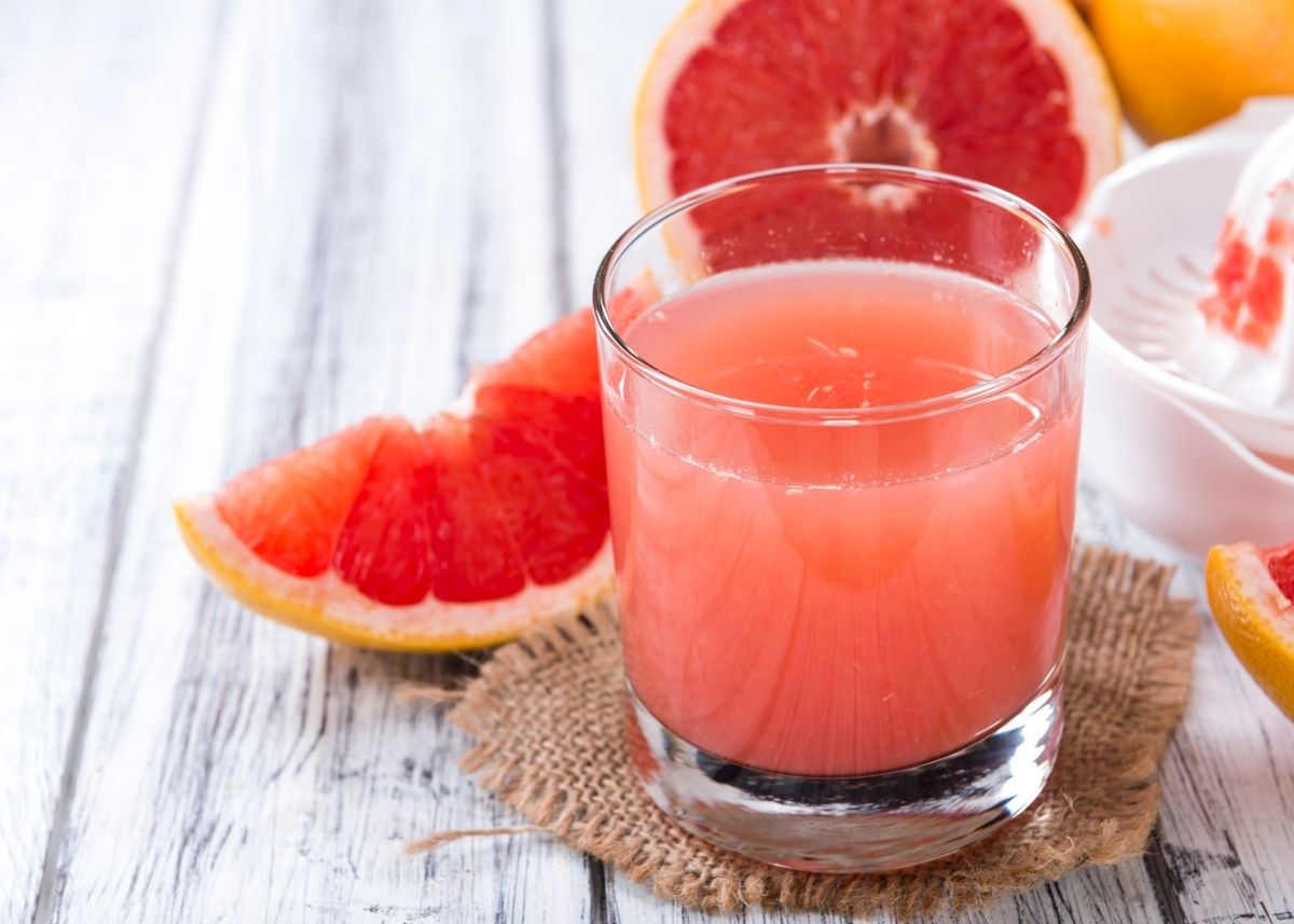 Small glass of grapefruit juice on a burlap coaster next to slices of grapefruit.