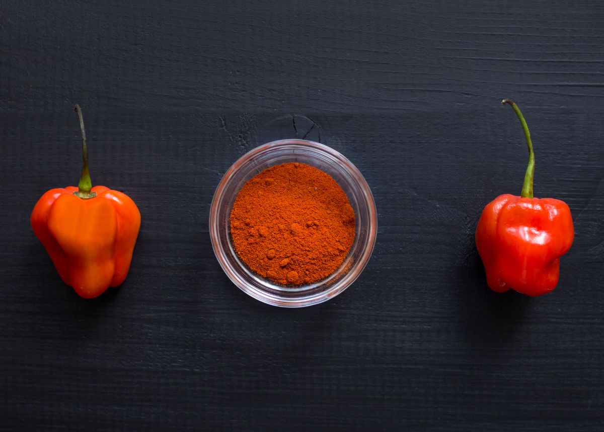 Two habanero peppers on either side of a small glass dish filled with pepper powder.