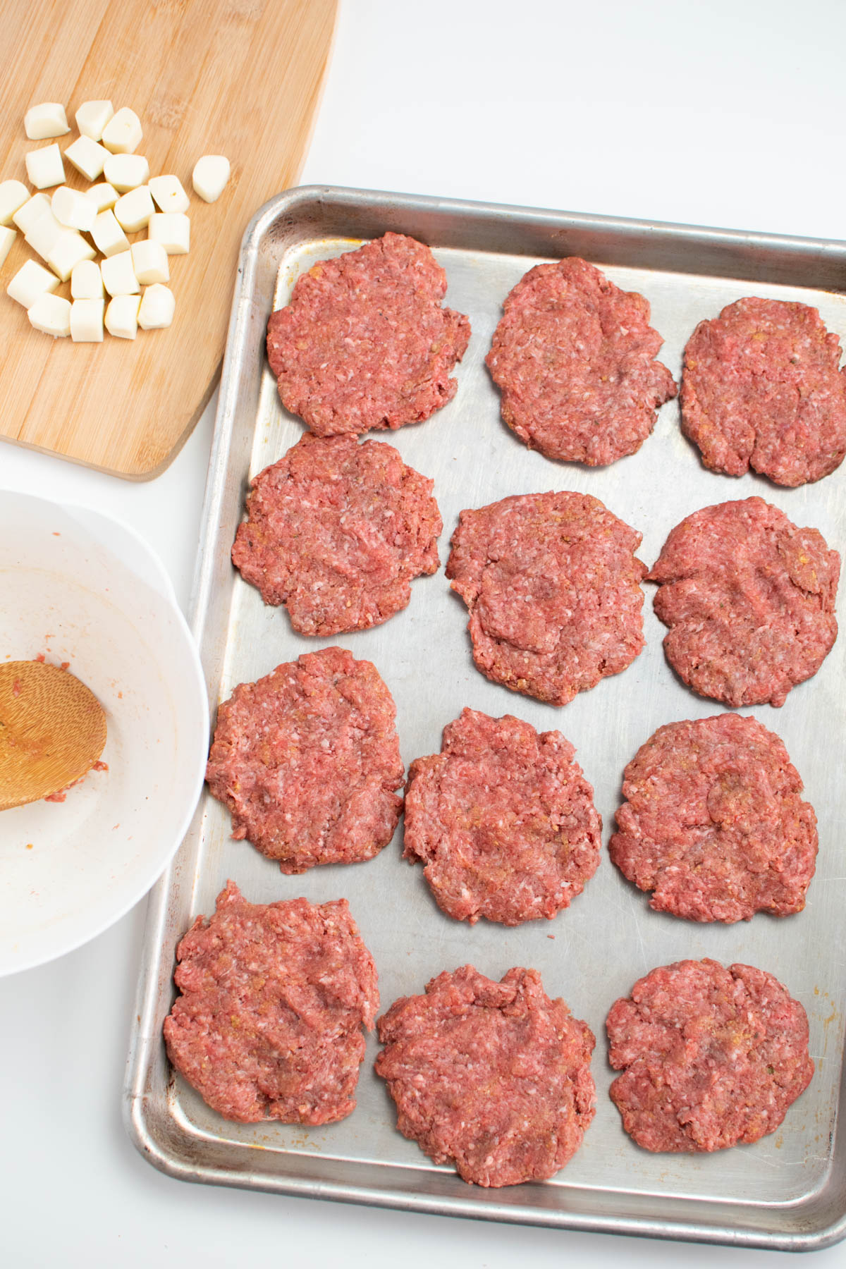 Twelve raw hamburger patties on metal sheet pan.