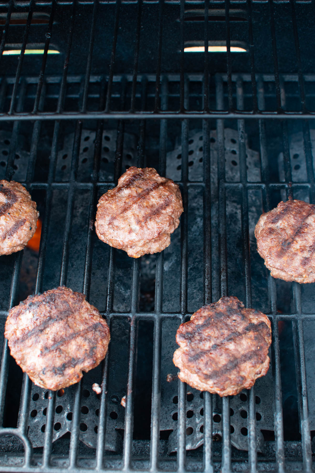 Five hamburgers on black grill with grill marks on them.