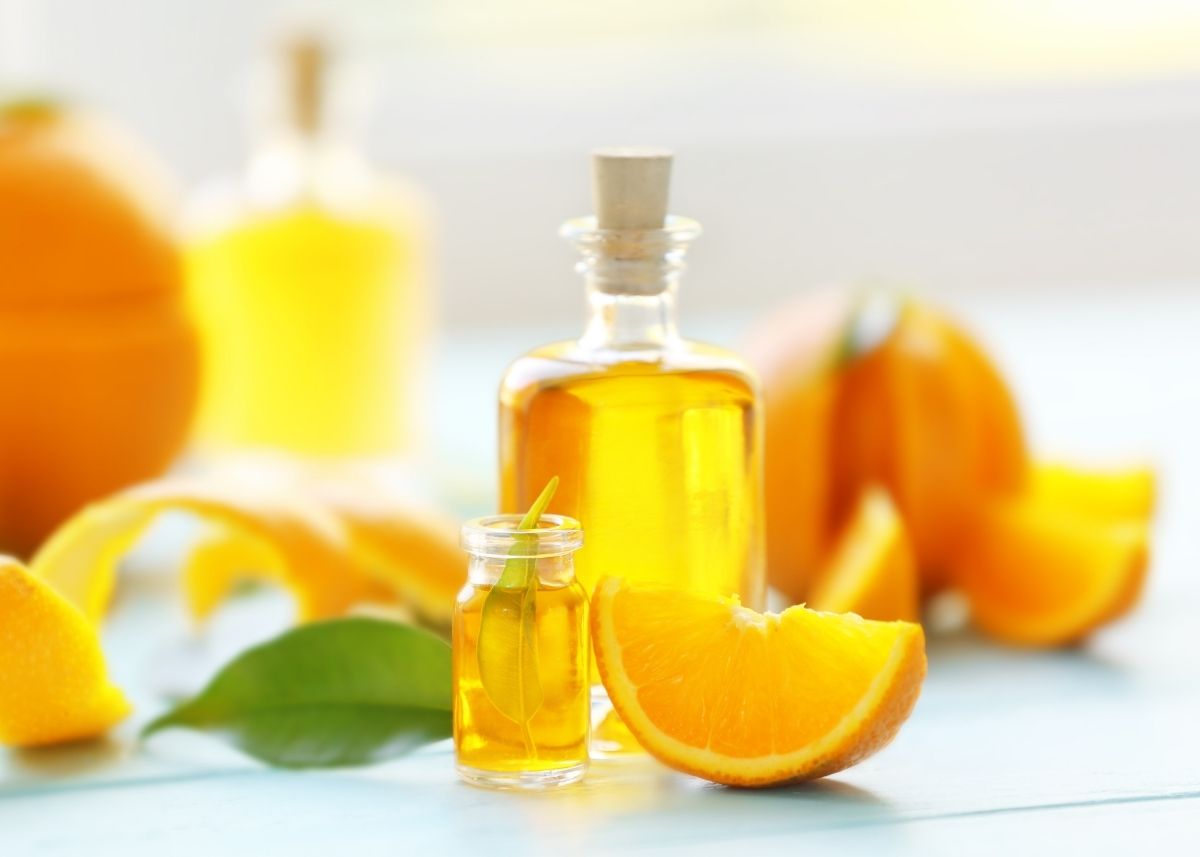 Two glass bottles of orange extract surrounded by whole and cut oranges on a table.