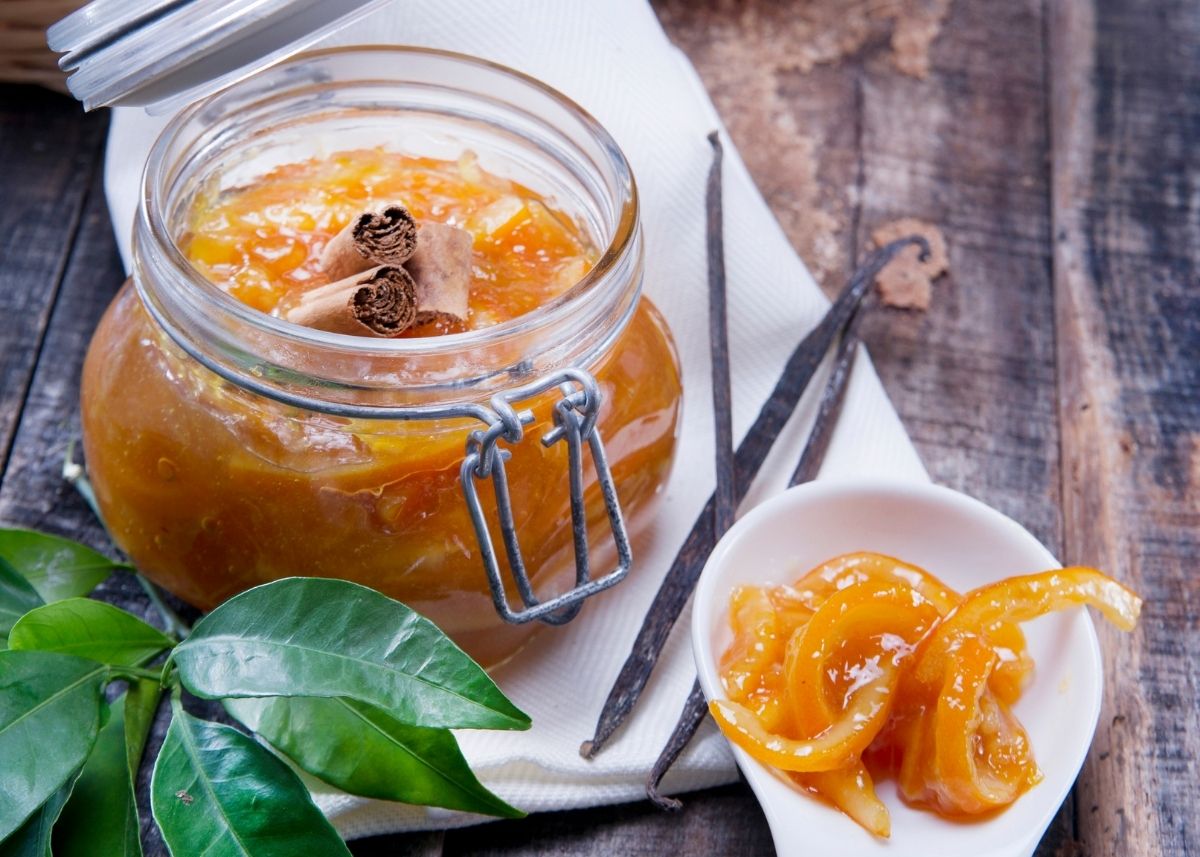 Small mason jar filled with orange marmalade next to green garnish on a wooden table.