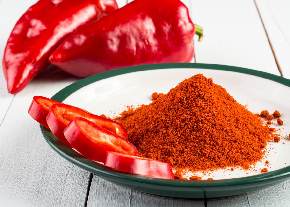 Whole and sliced red peppers and white bowl with blue rim filled with paprika powder.