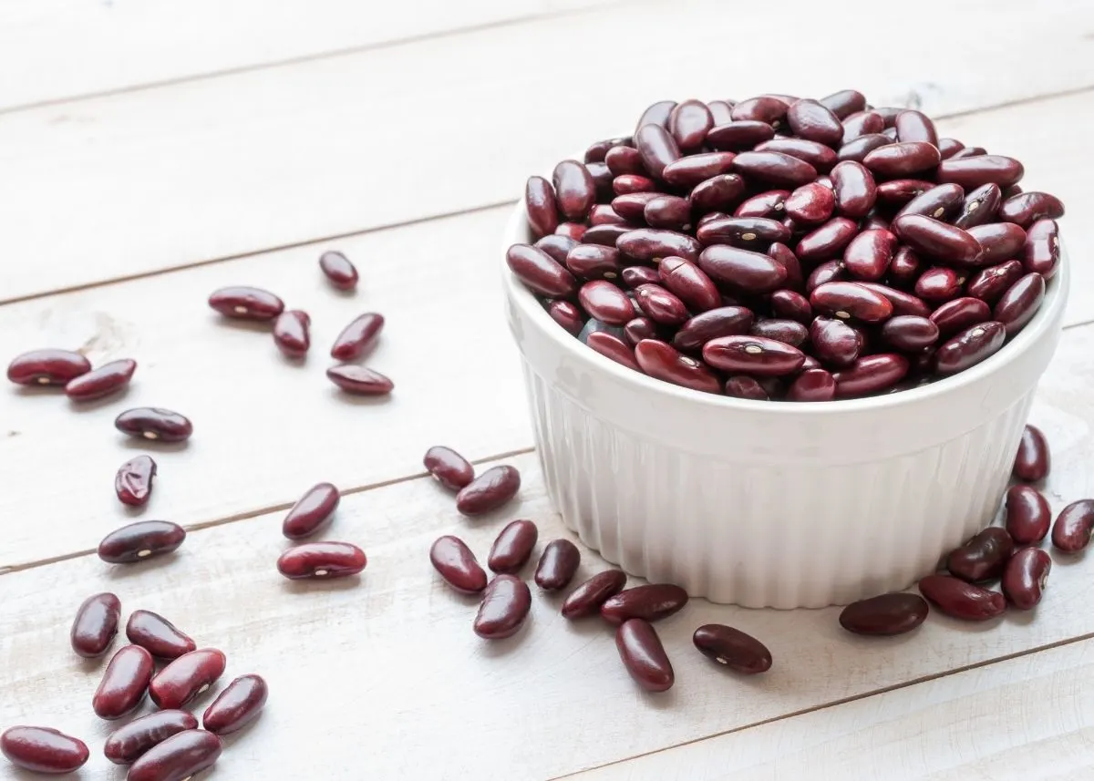 Dark red kidney beans in a white bowl on a white wood table.