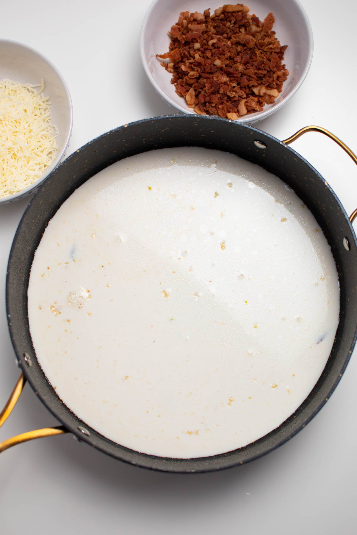 Cream sauce with minced garlic in large black skillet on white table.