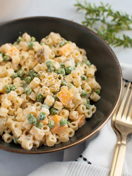 Bowl of dill pickle pasta salad with peas and cheese on table with gold forks nearby.