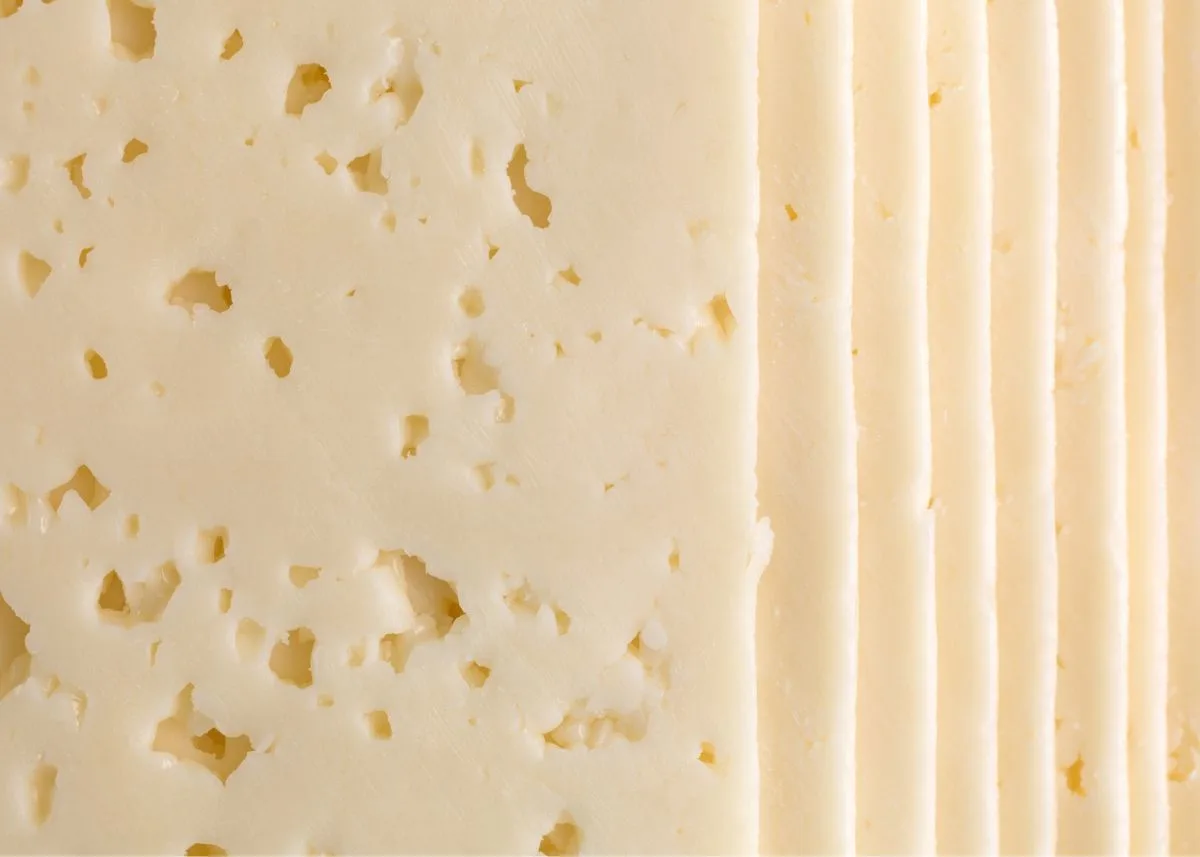 Close up view of several slices of white havarti cheese with holes.