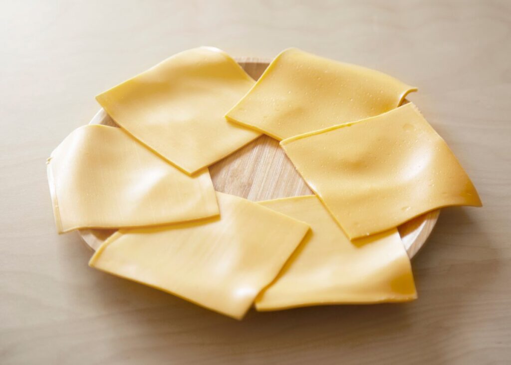 Several slices of homemade yellow American cheese on a round wooden plate.