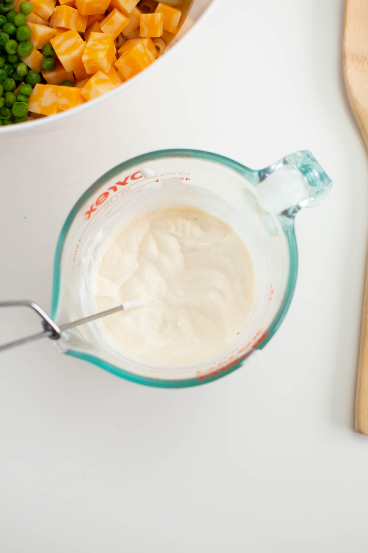 Mayonnaise and sour cream mixture in glass measuring cup with whisk.