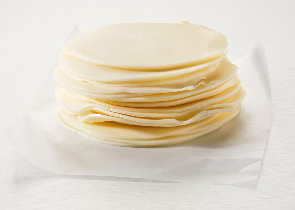Small stack of thinly sliced white provolone cheese on parchment paper.