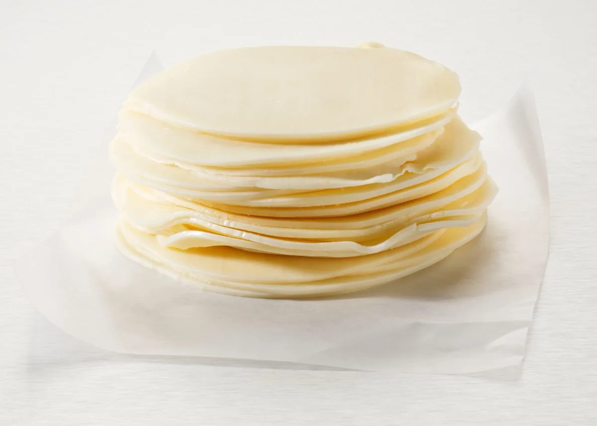 Small stack of thinly sliced white provolone cheese on parchment paper.