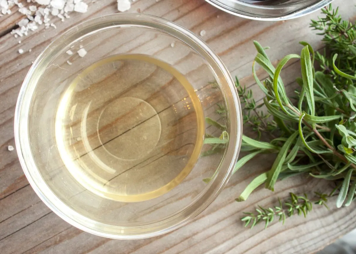 White wine vinegar in a small clear glass bowl next to green herbs.