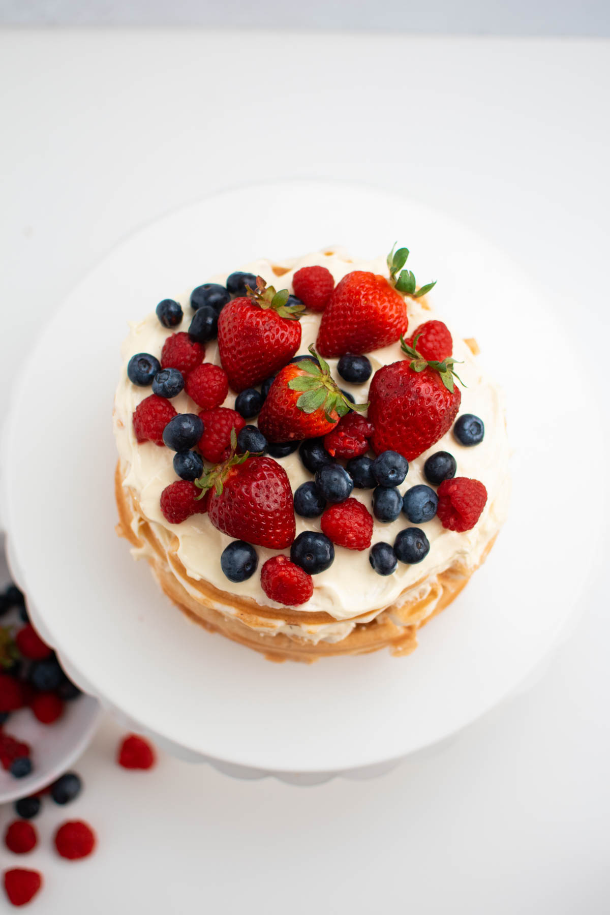 Various berries of vanilla waffle cake all on white cake stand.