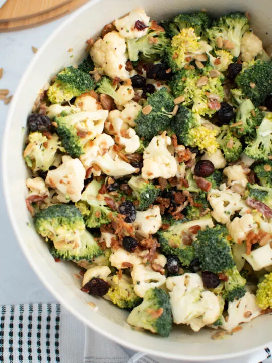 Broccoli cauliflower salad with cranberries, sunflower seeds, and bacon in white bowl.