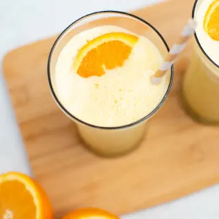 Orange Julius drink in glass with orange segment and striped straw.