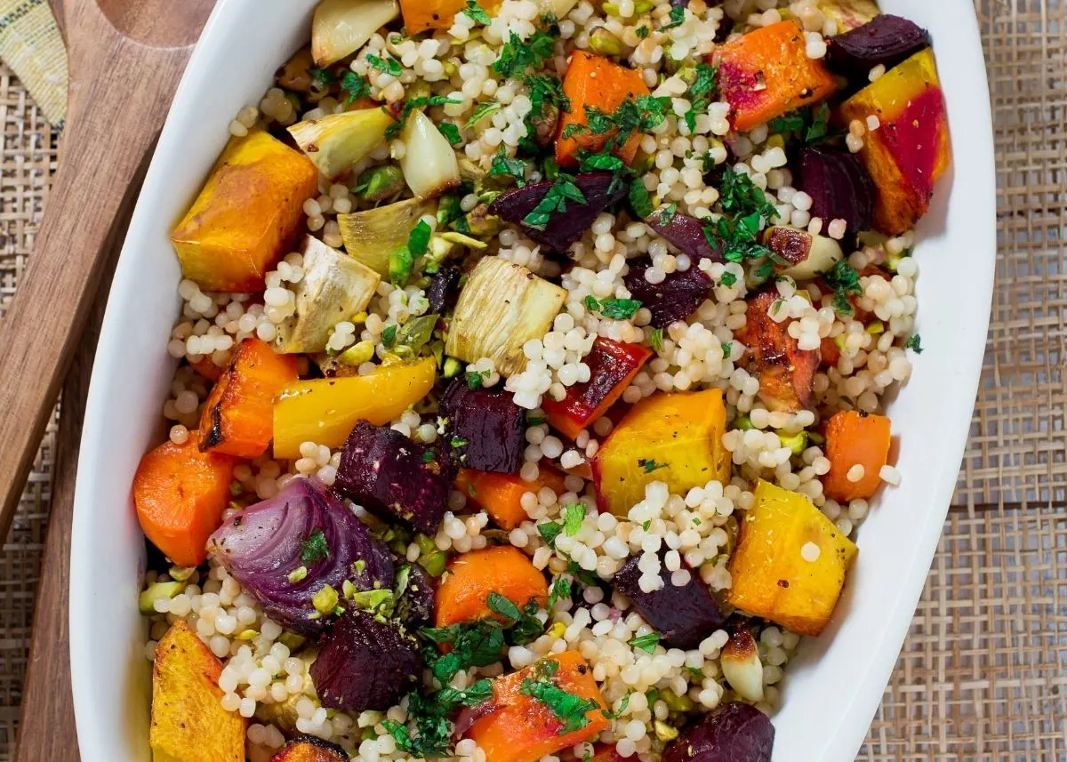 Couscous salad with herbs and roasted vegetables in a large white serving platter.