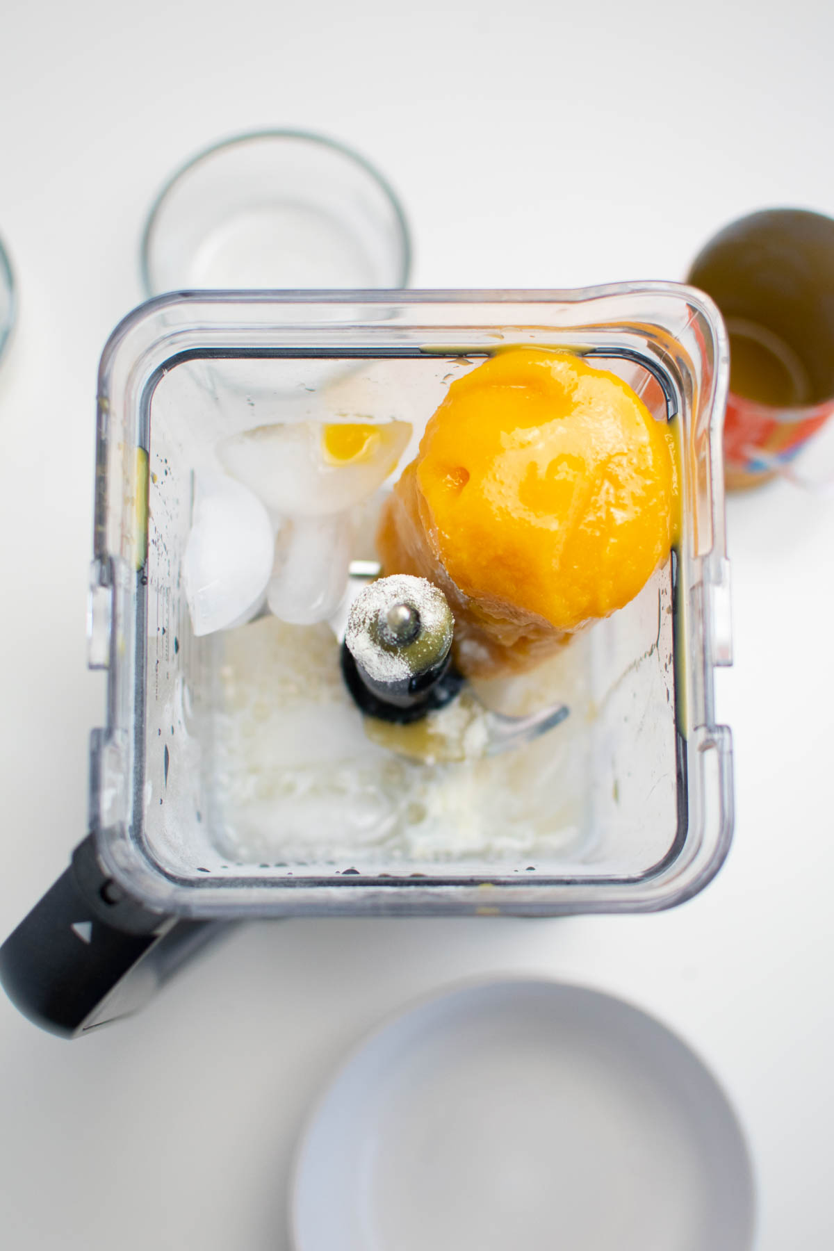 Frozen orange juice concentrate in blender with ice cubes, milk, and water.
