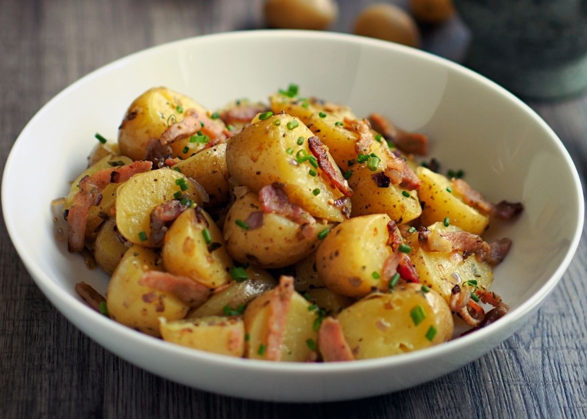 Warm German potato salad with bacon and herbs in a large cream serving bowl.