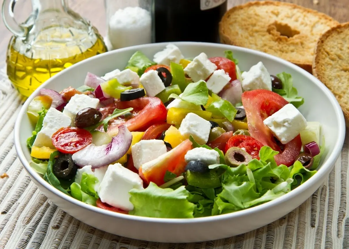 Greek salad with olives, tomatoes, feta cheese, and lettuce in a large white bowl.