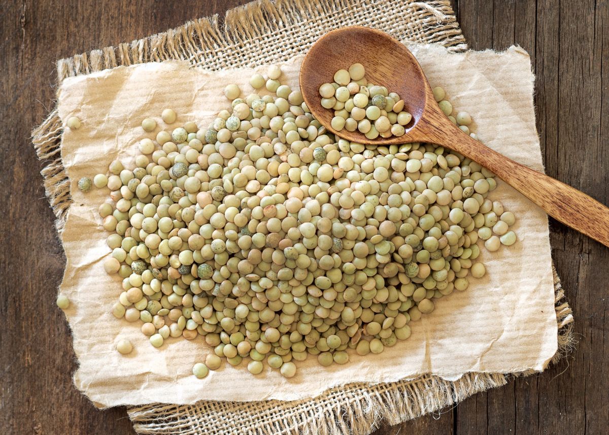 Large pile of green lentils on kitchen cloth with wooden kitchen spoon.