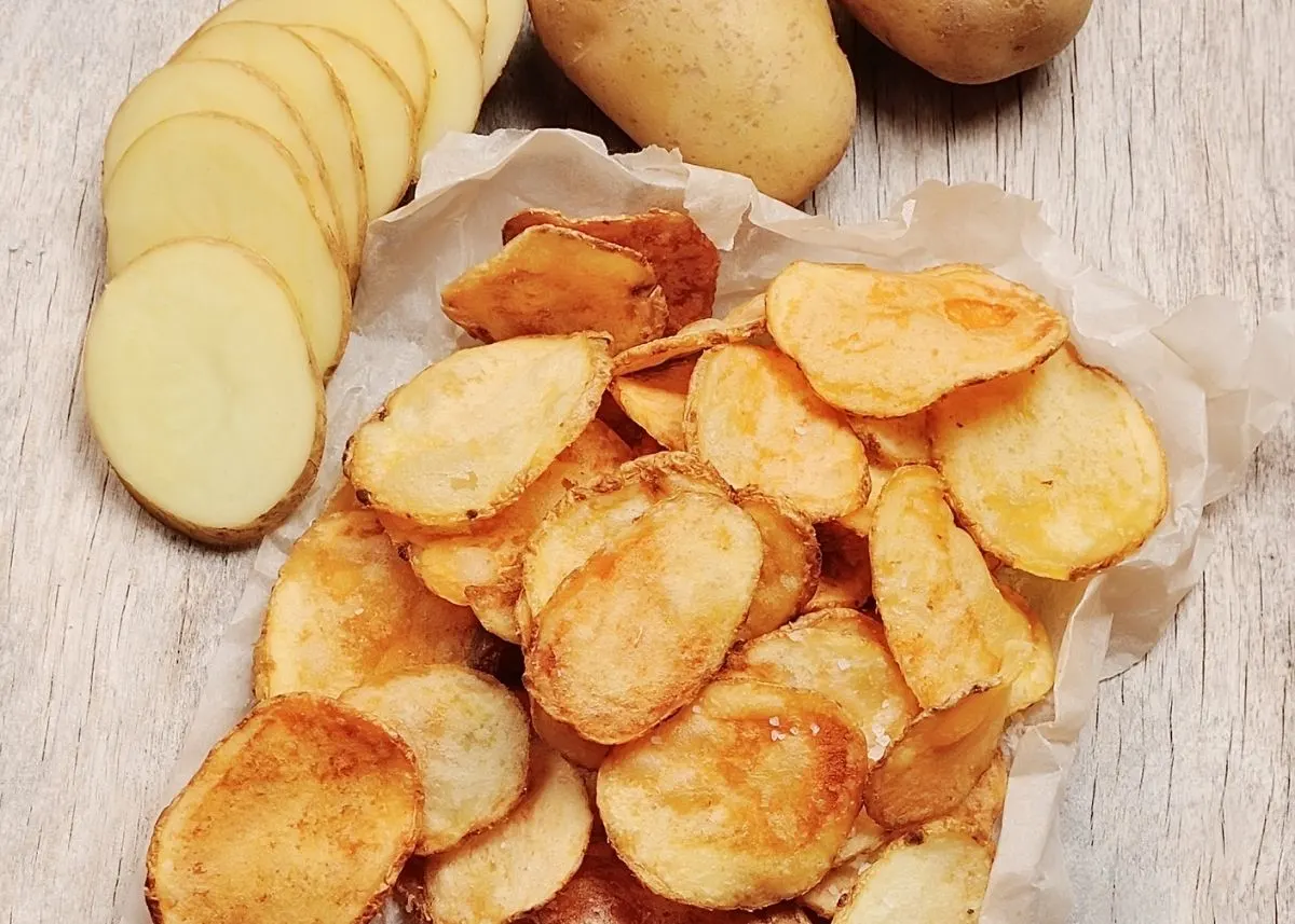 Sliced and whole potatoes next to pile of homemade potato chips.