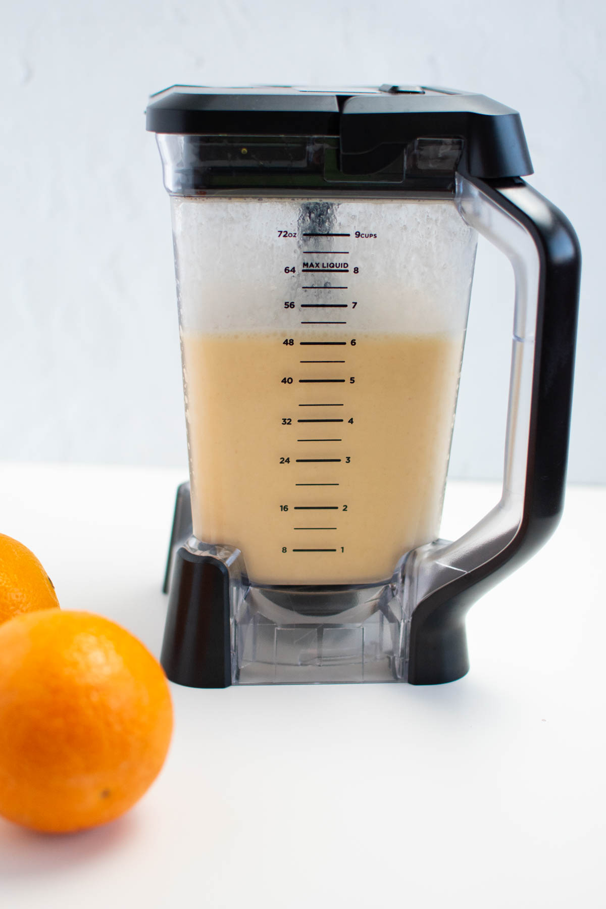 Orange Julius drink in blender with fresh oranges nearby.