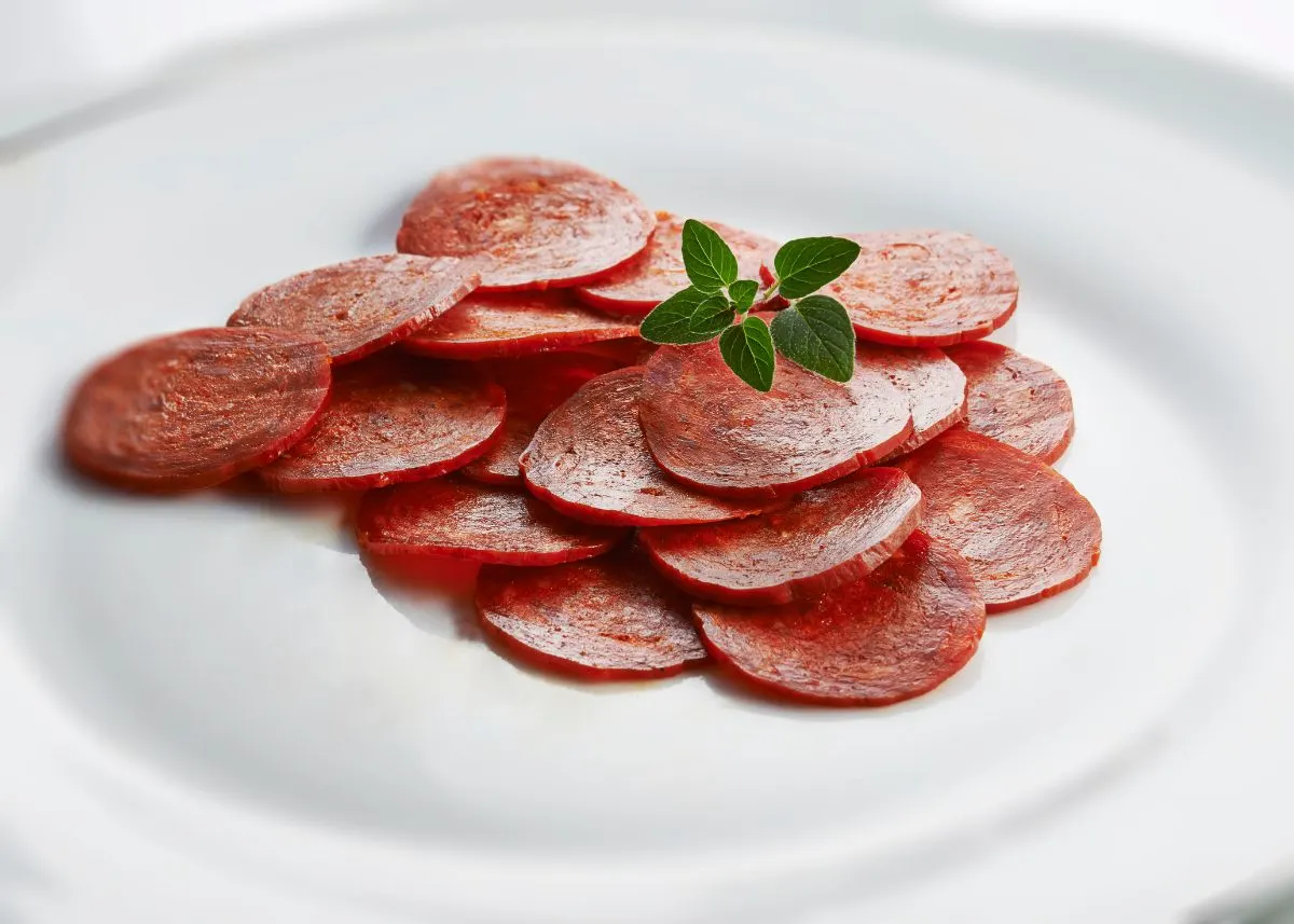 Slices of pepperoni spread on a white plate with green garnish on top.