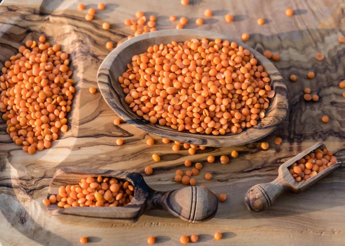 Red lentils in a large wooden bowl and rustic wooden scoop.
