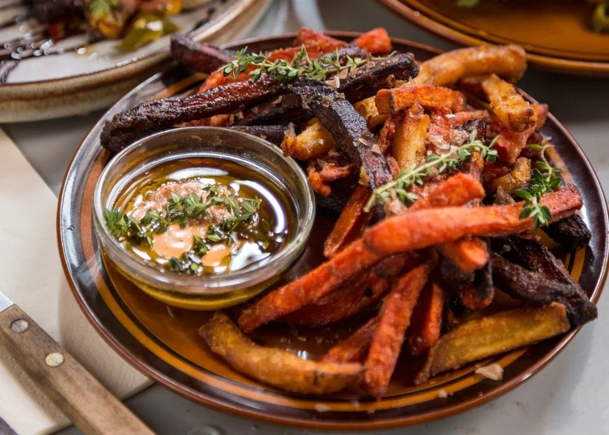 Roasted sweet potato fries with herbs and a dipping sauce in small glass bowl.