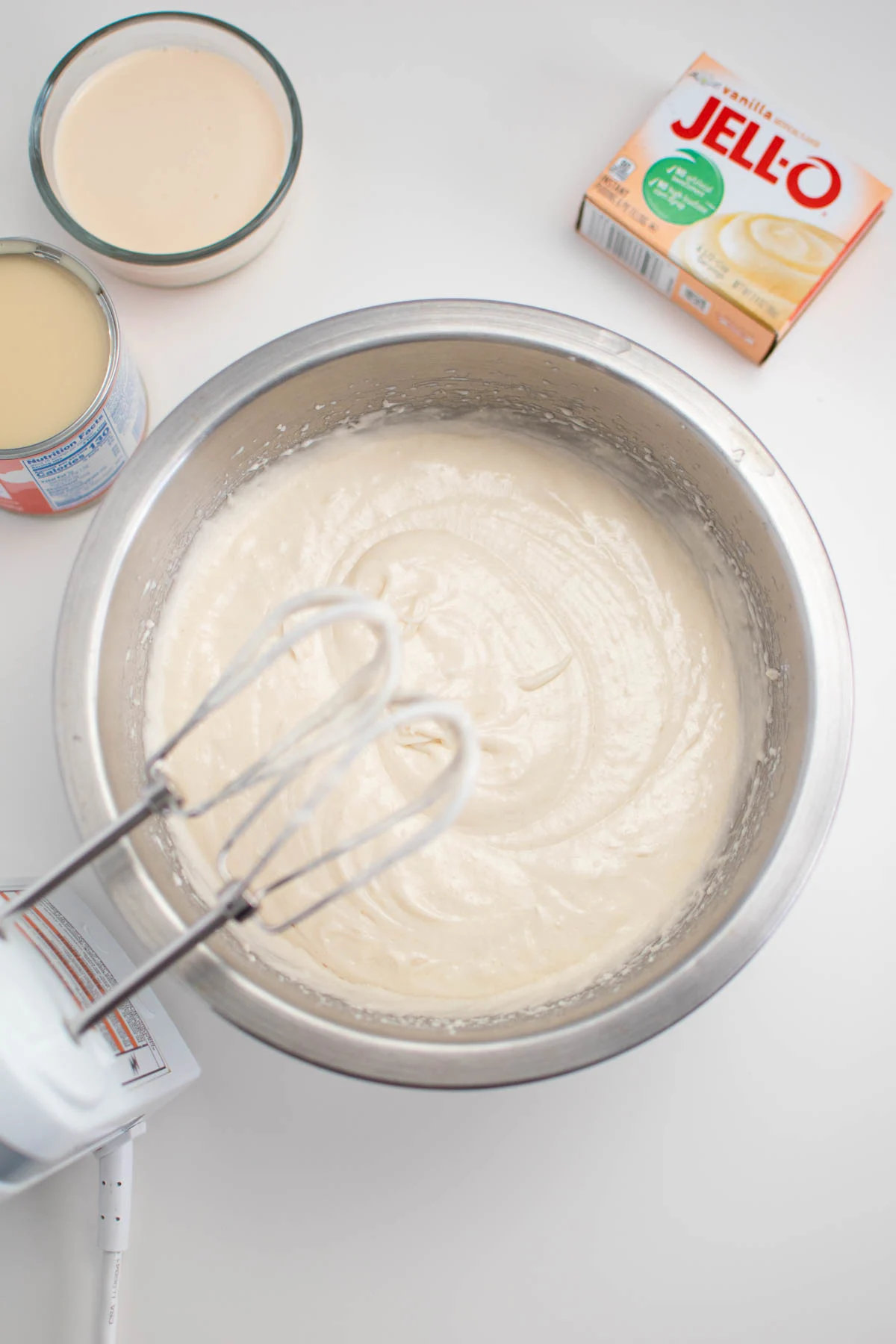 White cake batter in metal mixing bowl with beaters above.