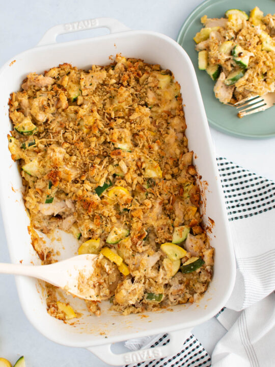 Chicken with Stove Top and zucchini casserole in white baking dish with wooden spoon and plate of casserole nearby.