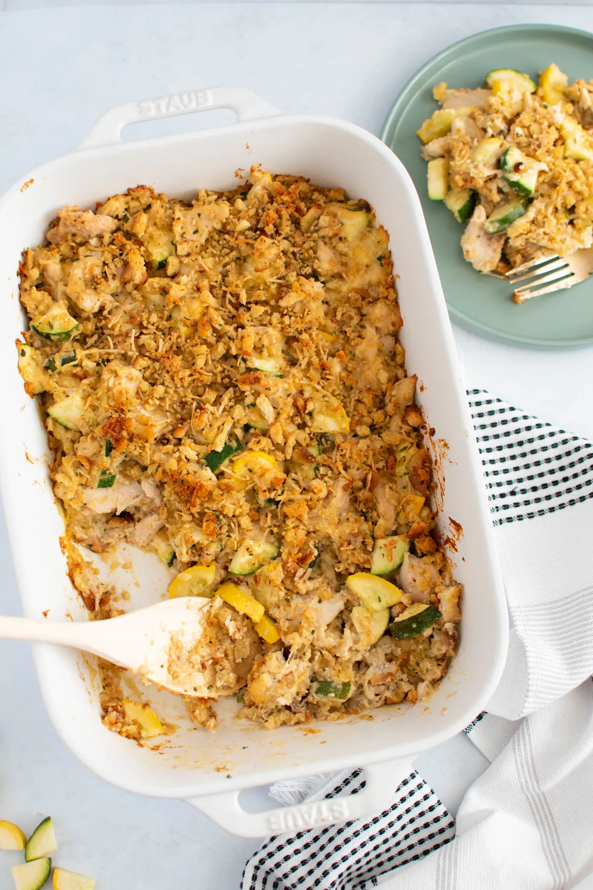Chicken with Stove Top and zucchini casserole in white baking dish with wooden spoon and plate of casserole nearby.