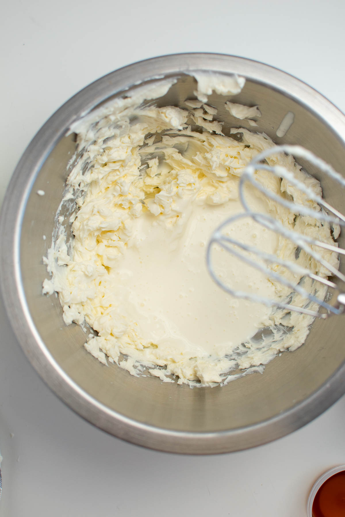 Cream cheese and heavy cream in metal mixing bowl with electric beaters over the bowl.