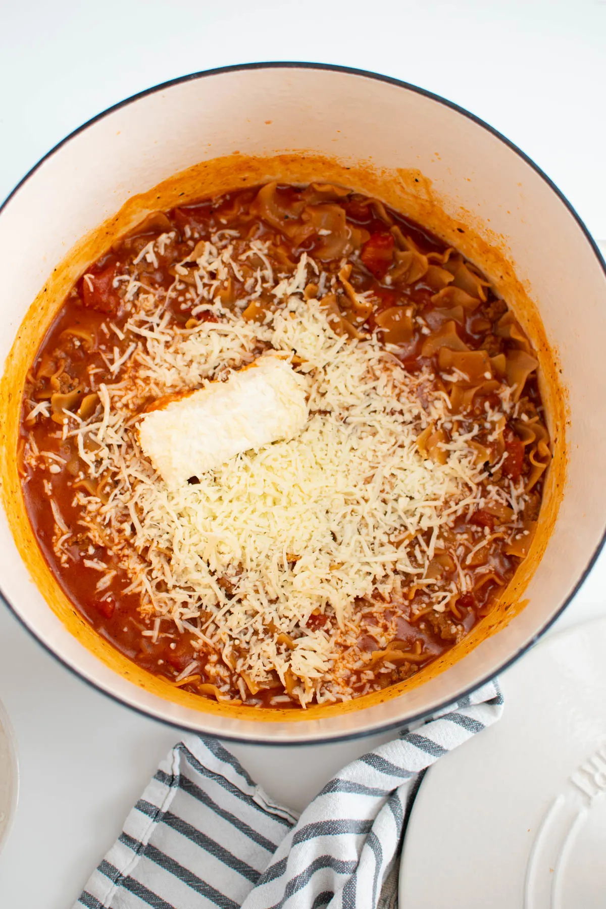 Block of cream cheese and shredded mozzarella in pot of meat sauce and pasta.