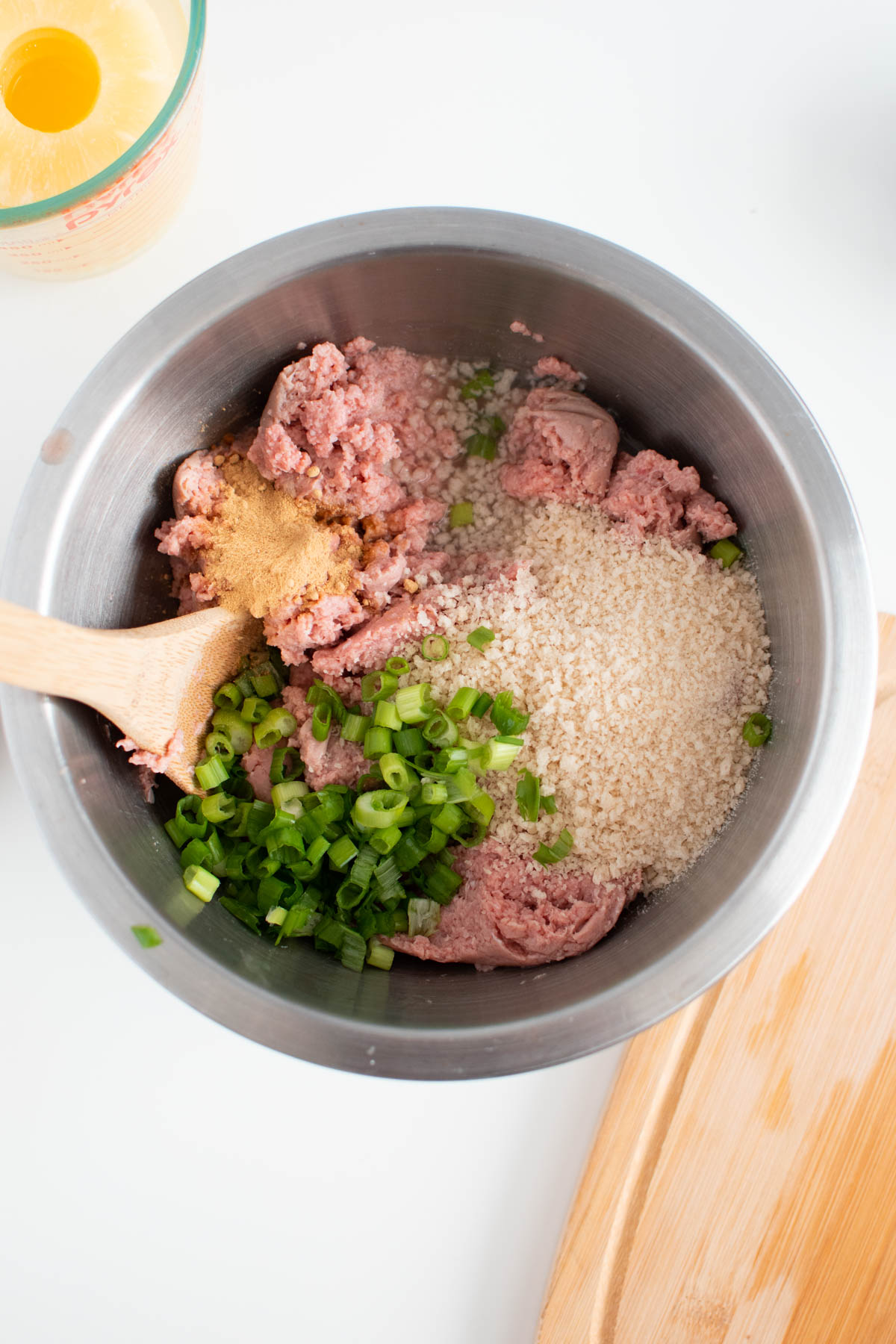 Raw ground turkey with green onion and breadcrumbs in metal mixing bowl.