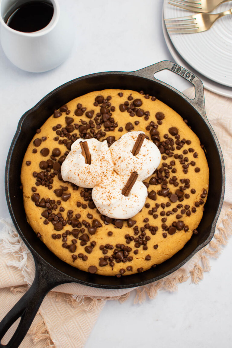 Pumpkin cast iron pancake with whipped cream pumpkins on table with syrup and plates in background.