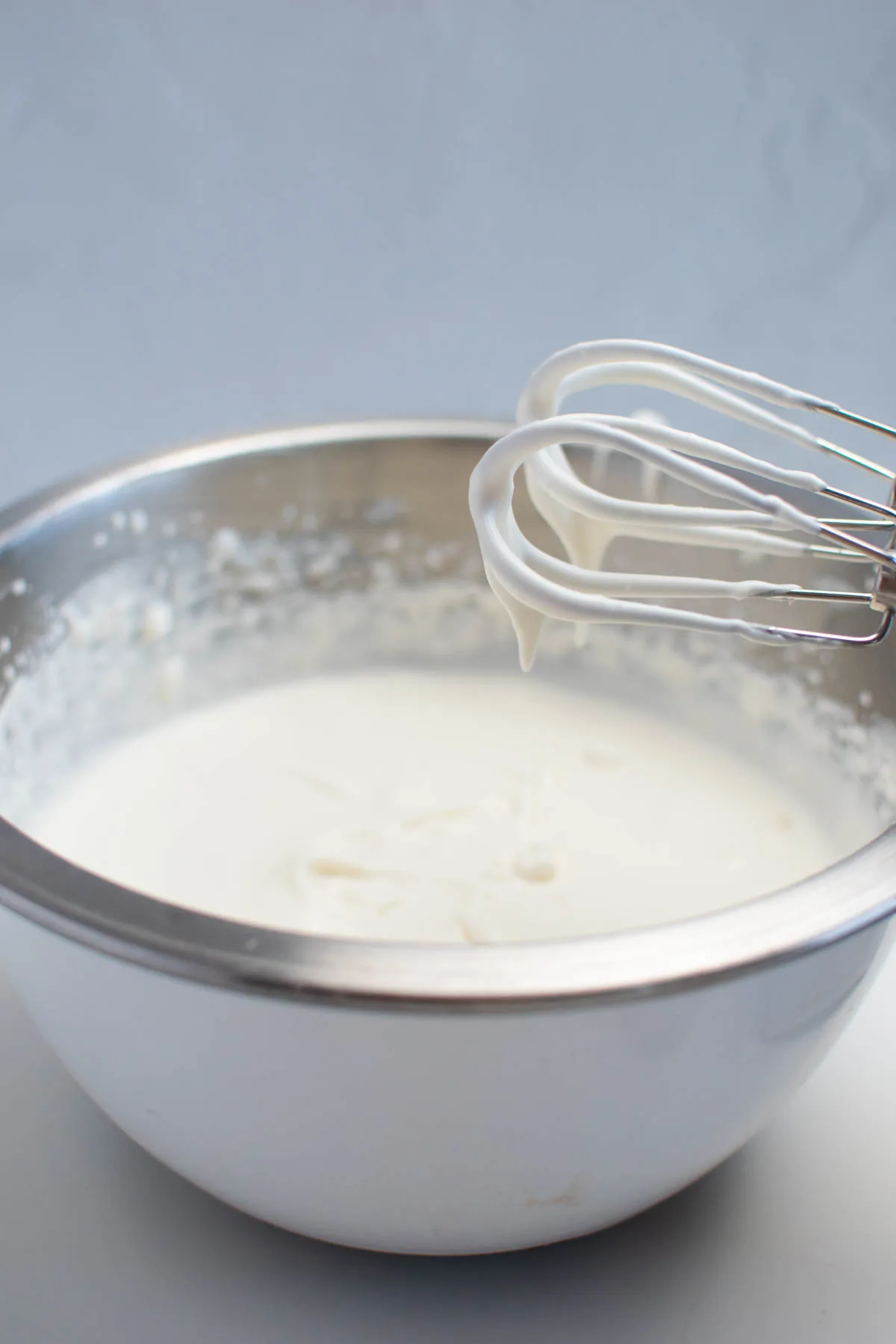 Electric beaters with soft peaks of whipped cream sit over metal mixing bowl.