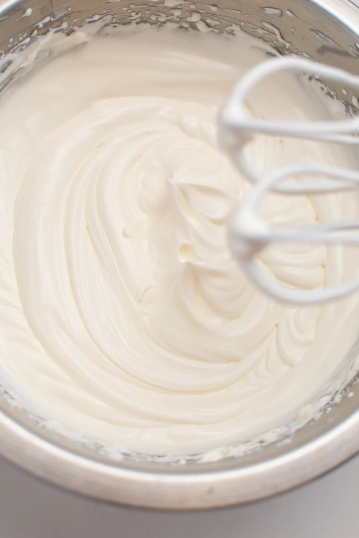 Stiff peaks in bowl of whipped cream with electric beaters overhead.