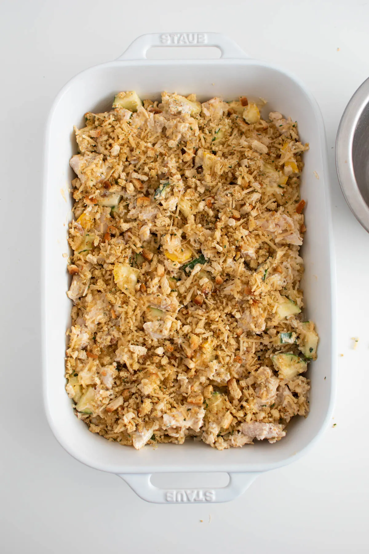 Unbaked chicken zucchini casserole in white baking dish on white table.