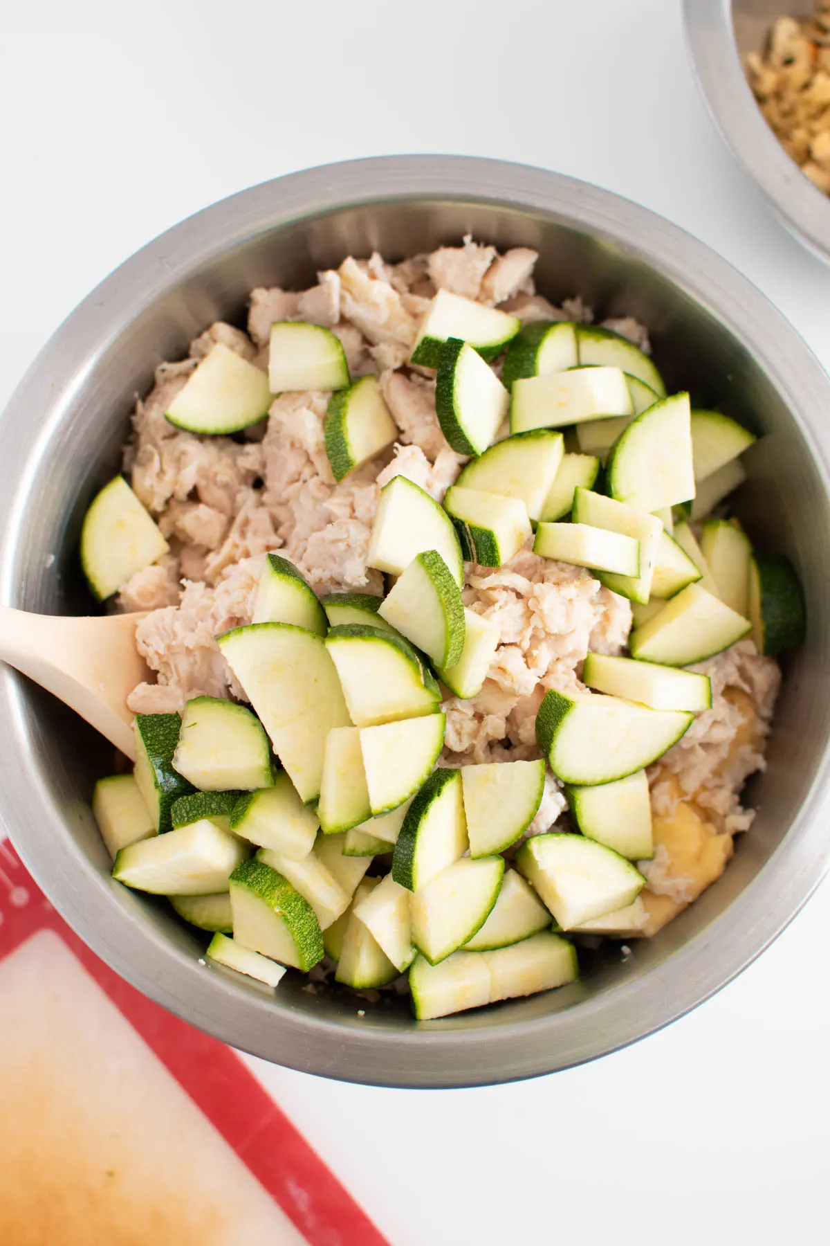 Diced zucchini and rotisserie chicken in metal mixing bowl with wooden spoon.