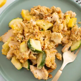 Zucchini casserole with chicken on green plate with gold fork and kitchen towel nearby.