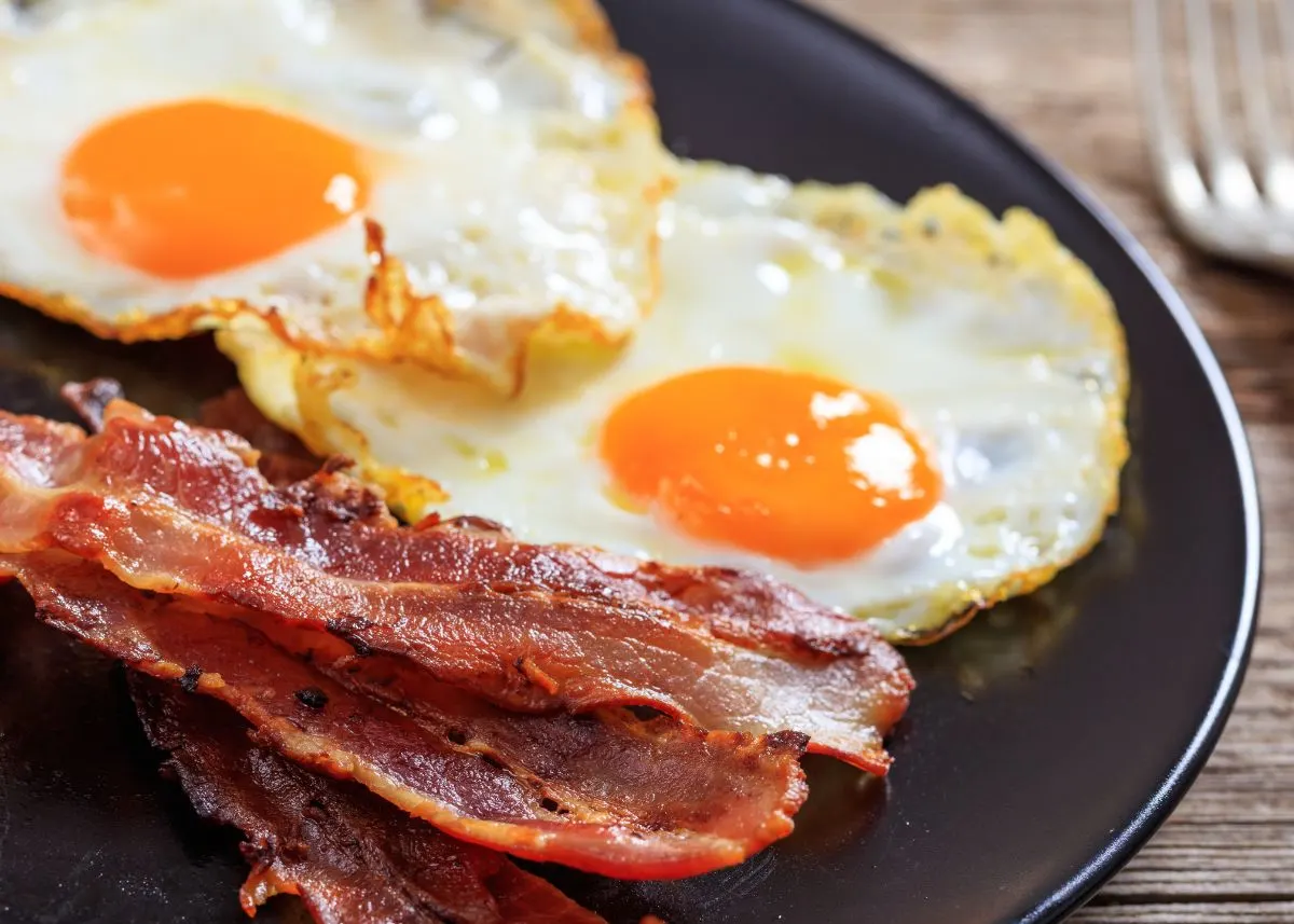 A plate with two sunny-side-up eggs and bacon next to fork.