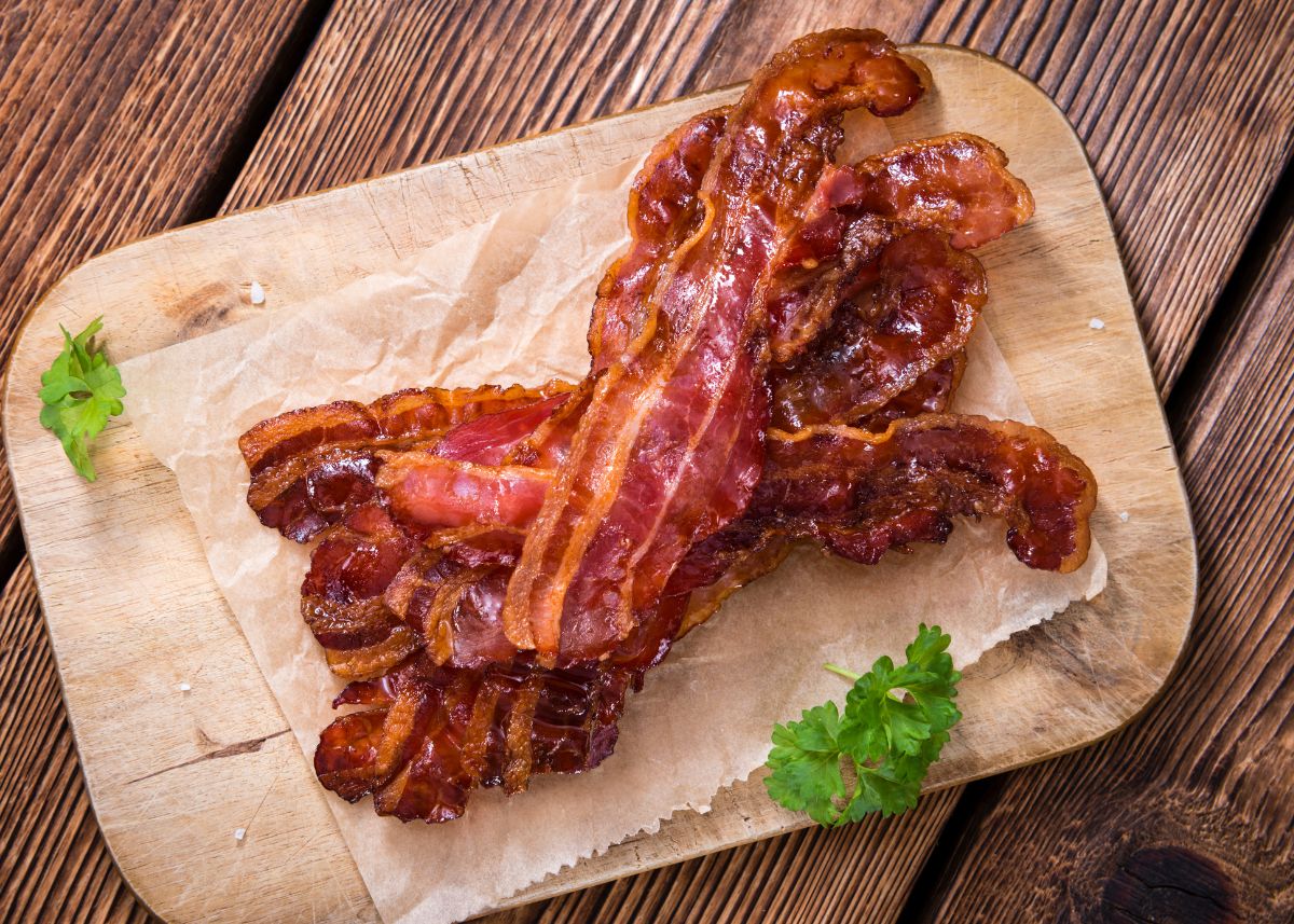 Several slices of cooked bacon on brown parchment paper with green garnish.