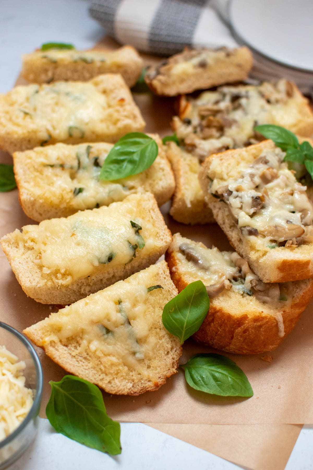 Pieces of cheesy bread with basil leaves on brown parchment paper.